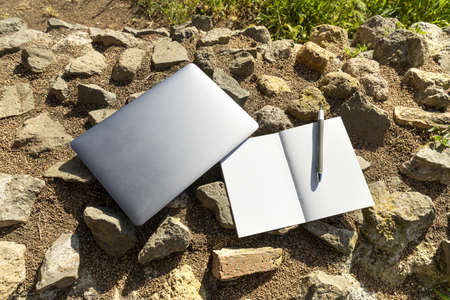 A laptop and an open note pad with a pen leayed on a stone wall in a park. Open air work conceptの写真素材