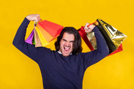 Hurray! A young man expressing his joy and satisfaction by raising his arms with lots of colorful shopping bags. Christmas shopping and sale conceptの写真素材