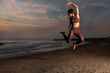 Young woman jumping at sunset on the beach expressing her joy of living. Late summer atmosphere.