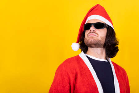 Young man dressed as Santa Claus has long hair and wears sunglasses. Yellow background and copy space for your message.の写真素材