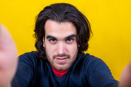 A young man with long hair and a beard takes a selfie. The man has a deep look.