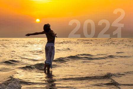 Beautiful woman in the water at the sea at sunset. The woman spreads her arms and embraces the...