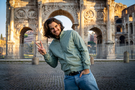 Happy moment in Rome. Young smiling man posing for a picture doing the V sign in front of the Titus...