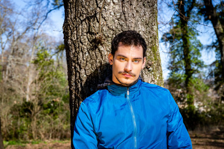 Portrait of a beautiful young man with blue eyes. The man is training in the woods and is leaning...