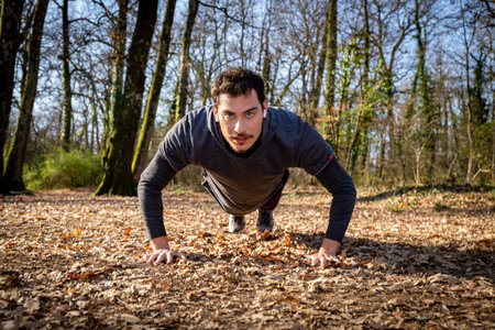 The runner is doing push-ups in the woods. The young man with the blue eyes and mustache is doing...