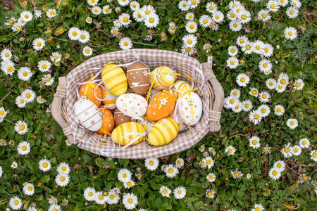Happy Easter! Basket with decorated Easter eggs. Multicolored Easter eggs among daisies in the garden.の写真素材
