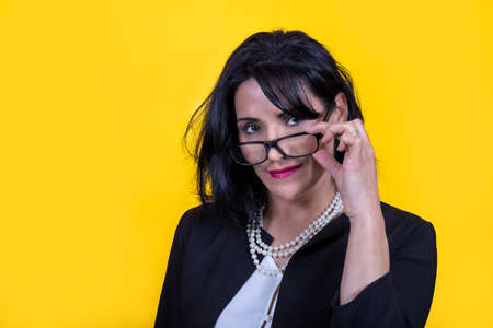 Young woman is taking off her eyeglasses. Beautiful brunette woman is wearing a black jacket and a pearl necklace.の写真素材