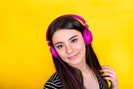Portrait of beautiful smiling girl with long hair. The young woman wears jeans and a striped t-shirt and uses headphones to listen to music.の写真素材
