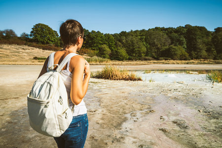 Young woman trekking to the Solfatara di Manziana (sulphurous area) in Italy. The woman is from behind and she is admiring the landscape.の写真素材