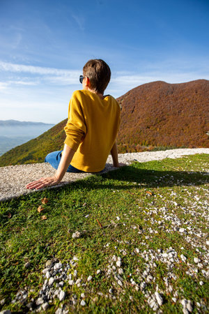 Young woman is sitting and looking at autumn landscape in Italy. Woman is sitting looking at the...