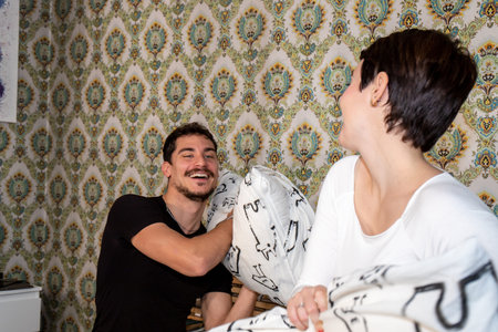 Young happy loving couple having a pillow fight in bed at home. Couple love and happiness concept.