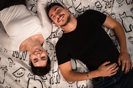 Beautiful couple are lying on the bed and looking at the camera. Young couple photographed from...