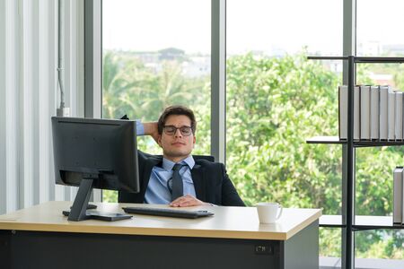 Businessmen in suits and ties rest their eyes after completing his quarter's sales estimates. Morning  atmosphere in a modern office. Take a nap at work.の写真素材