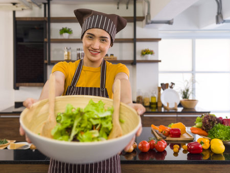 The housewife dressed in an apron and a hair cap, smiled and offered a salad bowl on the front....