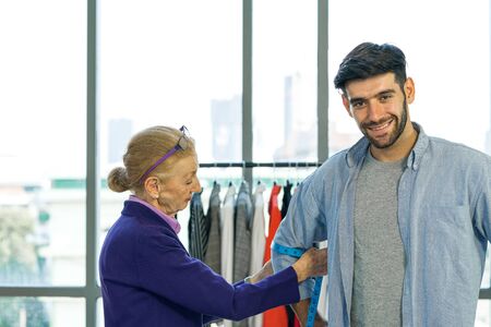 Man and woman working in home base cloth design business. Senior fashion designers measure the size of customers' arms. Young client is happy to have a new dress.の写真素材