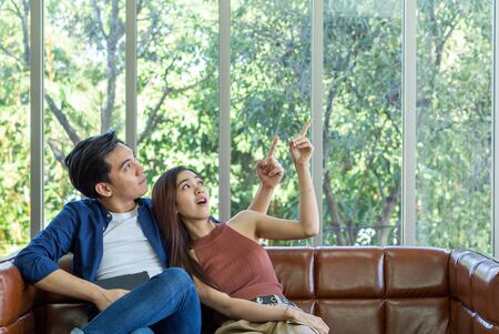 Young couples spend holidays in the living room. The young man wore comfortable clothes and the girlfriend pointed finger and looked in the same direction.の写真素材