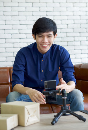 Young asian man talk to a customer about delivering products via application on mobile phone. Small home business concept.の写真素材