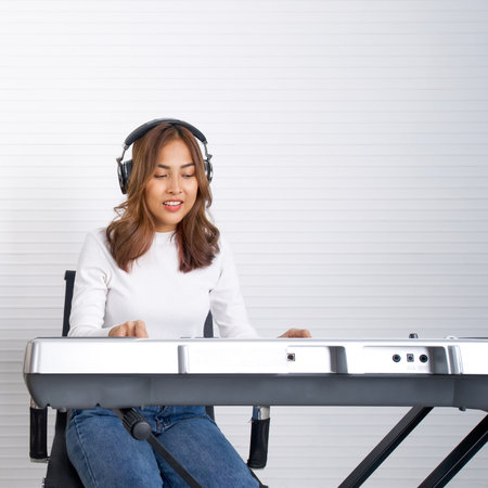 Young asian woman playing an electric keyboard in front of white walls. Musicians producing music in professional recording studio.の写真素材