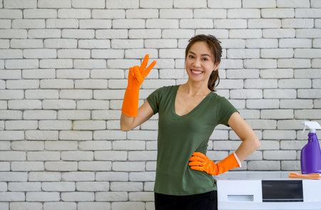 Asian maid wearing rubber gloves  stand on the waist beside the washing machine. Working atmosphere in the laundry room.の写真素材