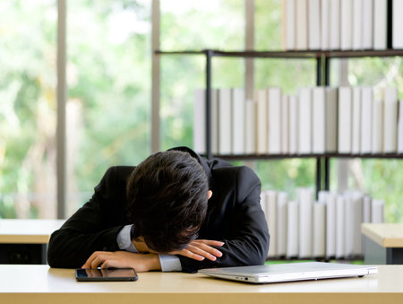 Young asian employee take a nap in the office on a table with tablet and laptop computer.の写真素材