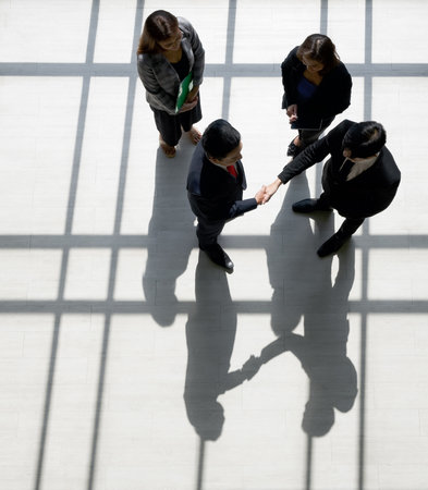 Business partners shaking hands in the modern office. Standing near the window while the sunlight shines on them. There is a shadow on the wooden floorの写真素材