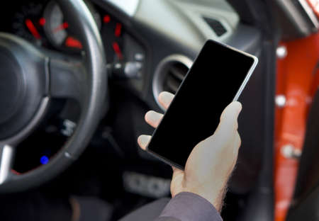 A blank screen mobile phone in the hand of a business man sitting in a sports car.の写真素材
