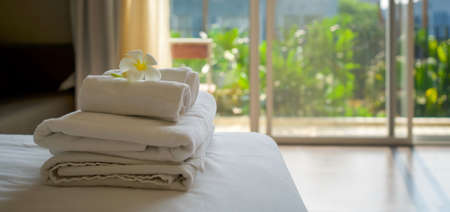 Two white towels on clean bed in hotel room with blurred background. Summer holiday and vacation concept.の写真素材