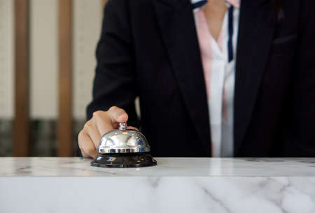 Closeup of a businesswoman hand ringing silver service bell on hotel reception desk.の写真素材