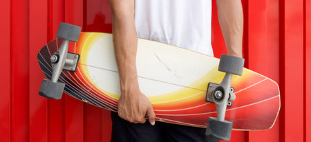 Closeup man's hand holding the surfskate board in hip position in front of red galvanized steel...