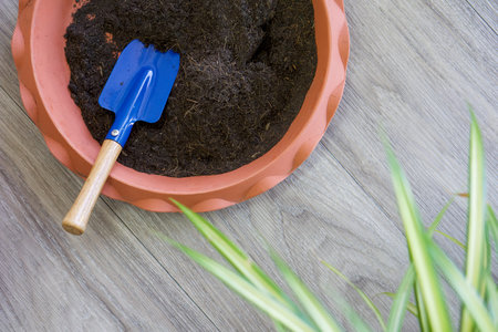 Blue gardening shovel in pot planters with soil and fertilizer on wooden floor. (Top View)