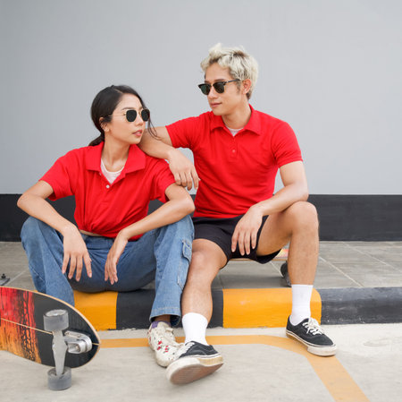 Asian couple resting after skateboarding. Young asian man in red T-shirt with collar and black...