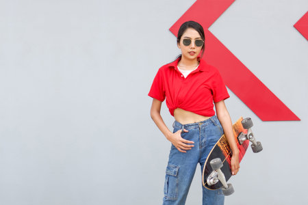 Young asian woman in red T-shirt with collar holding the surfskates board in hip position. While put...