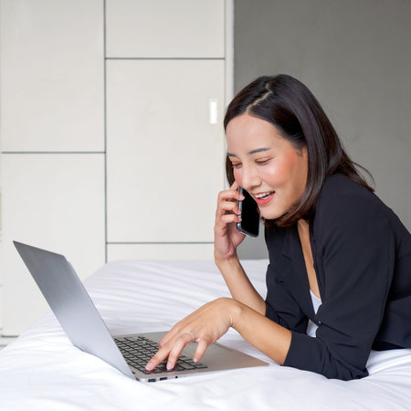 Young asian woman in black suit use the laptop computer and mobile phone to work in the morning in...