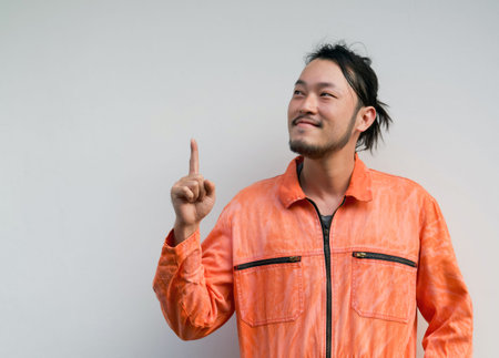 The chief mechanic in an orange uniform pointing one finger in upward direction. Portrait on gray background with studio light.の写真素材