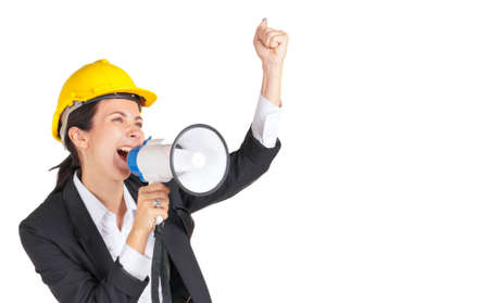 Caucasian businesswoman with a yellow construction helmet shouted at a megaphone while raising her fist over her head. Portrait on white background with studio light.の写真素材