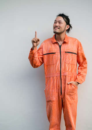 The chief mechanic in an orange uniform pointing one finger in upward direction. Portrait on gray background with studio light.の写真素材