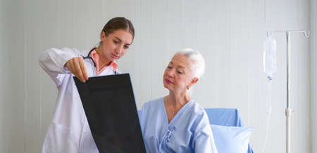 Senior female patient and doctor. Young doctor explained the examination results of the x-ray film to the elderly patients in the recovery room.の写真素材
