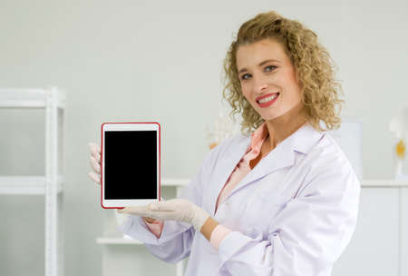 Young blonde scientist holding blank screen tablet computer. Working atmosphere in chemical laboratory.の写真素材