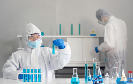 Epidemiological researcher in virus protective clothing look at  blue liquid chemicals in test tube....