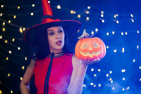 Caucasian woman in red dress holding pumpkin carved into a face, enjoy halloween party decorated with smoke fog and flashing lights.の写真素材