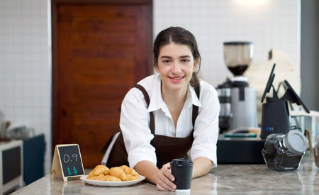 Young caucasian coffee shop staff dressed in brown apron handed a cup of coffee and croissant plate...