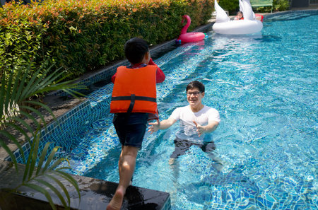 An asian dad take a vacation with his family in the pool, preparing to catch his son who will jump...