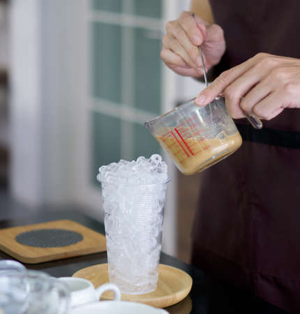 Clear plastic cup with ice for iced coffee on the table. Professional barista preparing coffee on counter.の写真素材