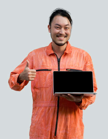 The chief mechanic in an orange uniform holding blank screen laptop computer. Standing with his finger thumbs up. Portrait with studio light.の写真素材