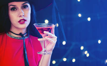 Caucasian woman in red dress holding martini glass with pink alcohol liquor, enjoy halloween party decorated with smoke fog and flashing lights.の写真素材