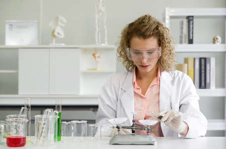 Young blonde scientist  measuring the chemicals for an experiment. Working atmosphere in chemical laboratory. Test tubes and beakers filled with chemicals on the table.の写真素材