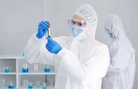 Epidemiological researchers in virus protective clothing looking at Blood samples of patients in test tube with screw cap.の写真素材