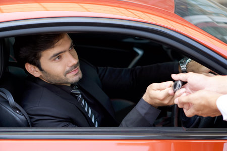 Young businessman in a black suit handling car key to the valet service staff while holding the car...