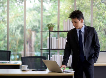 Young asian businessman in black suit use laptop computer to check email before go out to lunch break.の写真素材