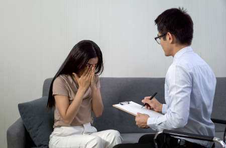 Sad woman with depression having consultation with psychiatrist in hospital mental health service centerの写真素材